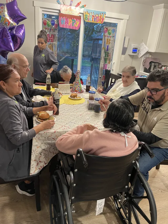 A birthday celebration at the dining table, with residents, family, and caregivers sharing a meal.