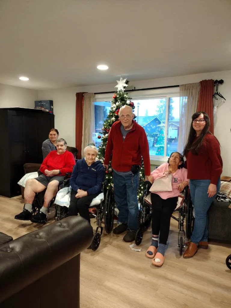 Residents, a family member, and caregivers gathered by the Christmas tree in the living room.